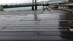 words in metal on a wooden boardwalk with the harbour in the distance