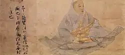 Three-quarter view of a seated man in a wide robe holding a stick like object. On the left there are three lines of text in Chinese script.