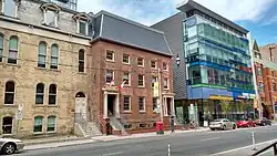Exterior facade of buildings on the north side of Adelaide Street. Two 19th century brick buildings to the left/west next to a 21st-century glass building.