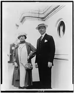 A well-dressed man and woman in 1920s clothing stand, apparently on a ship