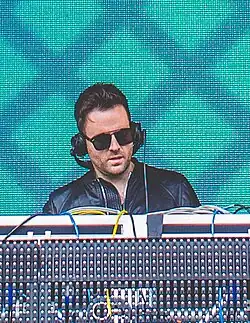 A dark-haired man performs on a set of turntables