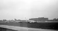 Small planes parked next to a runway, with terminal building in background
