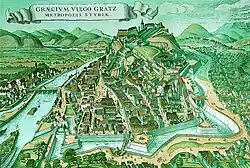 A fortress and houses on a hill which is surrounded by a river