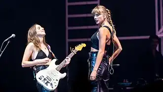 Haim and Taylor Swift in glamorous, industrial-inspired all-black outfits in a 2022 concert.