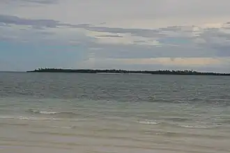 Small low green island in blue sea, at about two km. One beach can be made out.