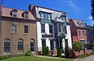 Three 19th-century brick houses attached at the sides. The one on the left is brown, the center one white and the right one red.