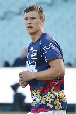 A man in a white shirt and maroon shorts stands on grass