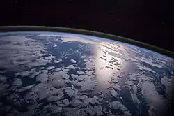 Image 20A view of Earth with different layers of its atmosphere visible: the troposphere with its clouds casting shadows, a band of stratospheric blue sky at the horizon, and a line of green airglow of the lower thermosphere around an altitude of 100 km, at the edge of space (from Earth)