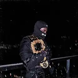 JPEGMafia in an identical black outfit carrying a wrestling belt