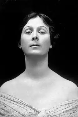 A black and white studio photograph of American dancer Isadora Duncan staring at a downward angle with an imperious air. Her shoulders are bare, and her dress has a decolletage neckline.