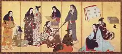 Nine women and a girl dressed in kimonos. One woman is reading a sheet of paper, another is playing a shamisen. One woman is doing the hair of another woman.