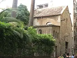 Church-like stone building, with vegetation along a tall iron fence