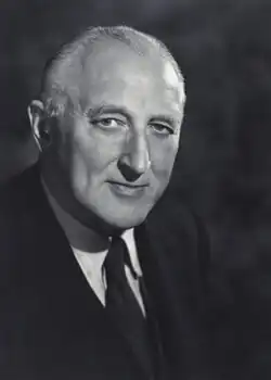 An older man, with short receding hair, in a formal black suit