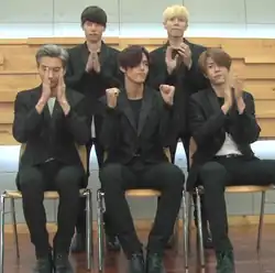 Three men sit in chairs with two men standing above them