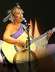 female caucasian with hair tied up with a bow holding an acoustic guitar and singing into a mic