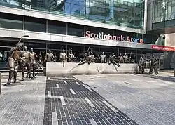 Statues of hockey players in front of a granite bench. The glass facade of Scotiabank Arena is in the background.