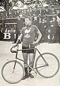 A man in a cycling uniform standing beside his bicycle on a racetrack