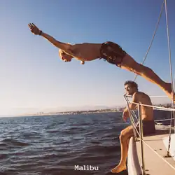 The image features the band members on a boat, in the ocean with a clear blue sky. Rocky is sitting on the edge and Ross is halfway jumping in the air.