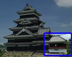 A one-storied structure with a veranda with red handrail connected to a two-storied castle tower. Both are located on a platform of unhewn stones.