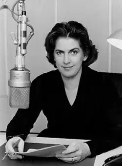 A woman sits in front of a mic, holding some papers.