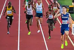 Frontal photo of Jakob Ingebrigtsen raising his hand after finishing ahead of eight other runners