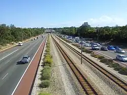 A railway line in the median strip of a freeway viewed from a bridge