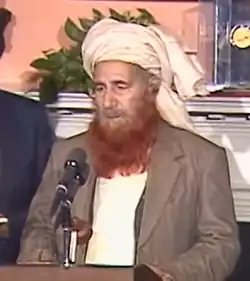 Headshot of a bearded Khalis in front of a light pink background