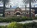 Former ground level station building on heritage display, with the landscaping of plants and palm trees fully grown, November 2024