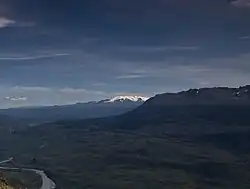 A glaciated, flat-topped, gently-sloping mountain with a much lower barren mountain in the right foreground.