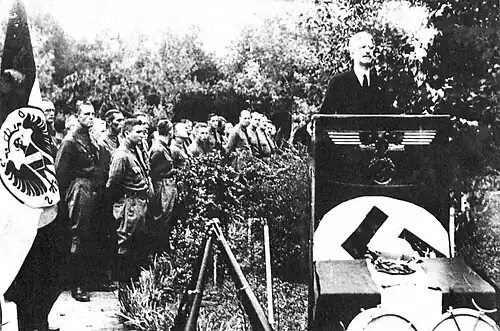 An assembly flanked by a flag of a shielded, phoenixlike bird