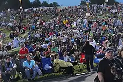 A crowd of people sitting on grass and in folding chairs