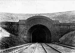 A black and white image of a rounded tunnel entrance with two tracks disappearing into the tunnel