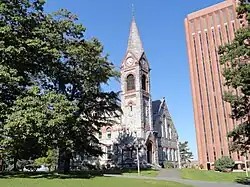 A building with a steeple in the foreground with a brick-clad structure in the brackground