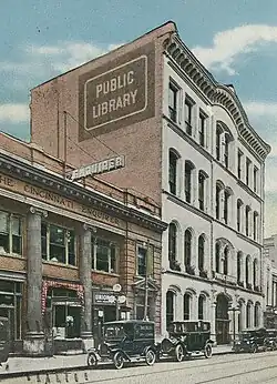 Colored photograph of the facade of the Old Main Library, with vintage cars in the foreground