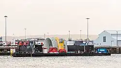 Twin hulled barge moored at a quayside, between the hulls is the top of an OpenHydro turbine, but only the outer shroud is visible,