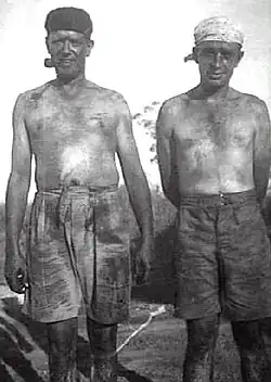 Two men stripped to waist and covered in coal dust, one smoking a pipe