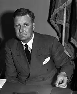 Sillitoe sitting at a desk wearing a suit.