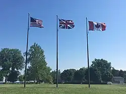 Flags of Canada, the United States, and the United Kingdom fly next to the memorial at equal height.