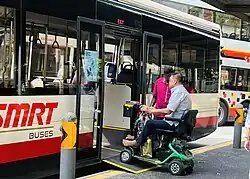 A man on a motorized wheelchair is using a ramp to enter an SMRT bus