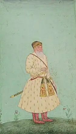 An old man with a white beard, wearing a cream jama, with a gold-leaf design