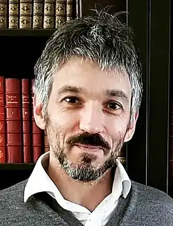 Headshot of Rémi Mathis standing in front of a bookshelf. He is a middle-aged man wearing a grey collar sweater.