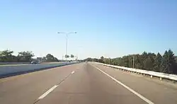 Ground-level view of two lanes of a divided freeway; the opposing lanes of traffic are separated by a narrow concrete barrier. A dense forest is visible to the left.