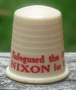 Beige thimble with red lettering, the visible part of which says "Safeguard the A..." and "NIXON for U...