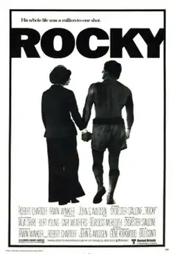 In a black-and-white poster, Rocky in his boxing outfit is holding hands with another person. The tagline above the film's title reads "His whole life was a million-to-one shot." The film's credits are printed below the poster.