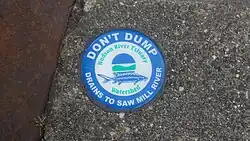 A blue and green circular medallion on a sewer warning that the discharge goes into the river
