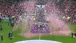 Confetti rains around a platform in the middle of a football pitch
