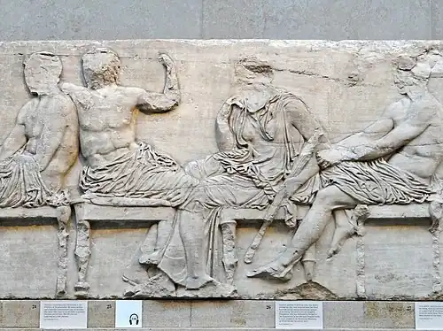 Four large, seated figures, with faces missing