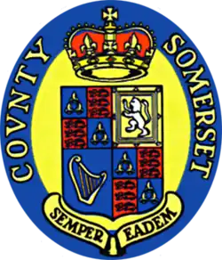 An oval seal featuring a shield on a yellow background with a blue border