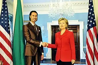 Photograph of Secretary of State Clinton meeting with Mutassim Gaddafi of Libya. She is standing on the right, he is on the left. Flags of both countries border the pair.