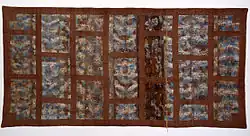 A piece of rectangular textile with thick brown stripes tiling the surface in rectangular multi-colored pieces.